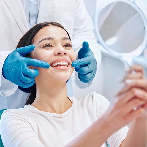 Dentist touching corner of woman’s cheeks as she smiles into mirror