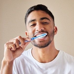 Man in white t-shirt brushing teeth with standard brush
